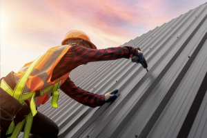 Photo of a roofer expertly installing a metal roof on a commercial building. The image captures the professional at work, securing metal panels under a clear sky, demonstrating precision and expertise in commercial roofing.